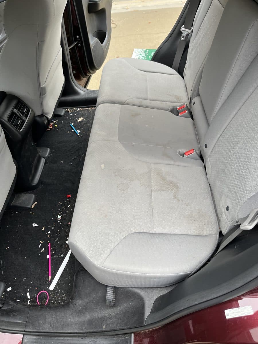 Back seat before detailing, stained cloth seat and debris on the floor